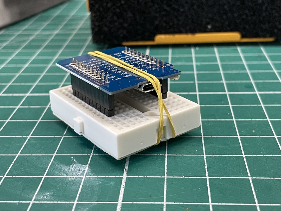 Small breadboard with a mounted breakout board, secured by a rubber band on a green cutting mat.