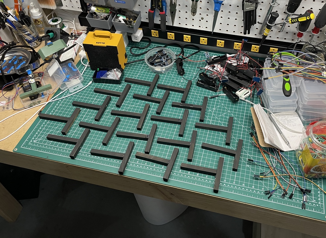 A green cutting mat with multiple black-painted, T-shaped wood pieces arranged in a pattern.