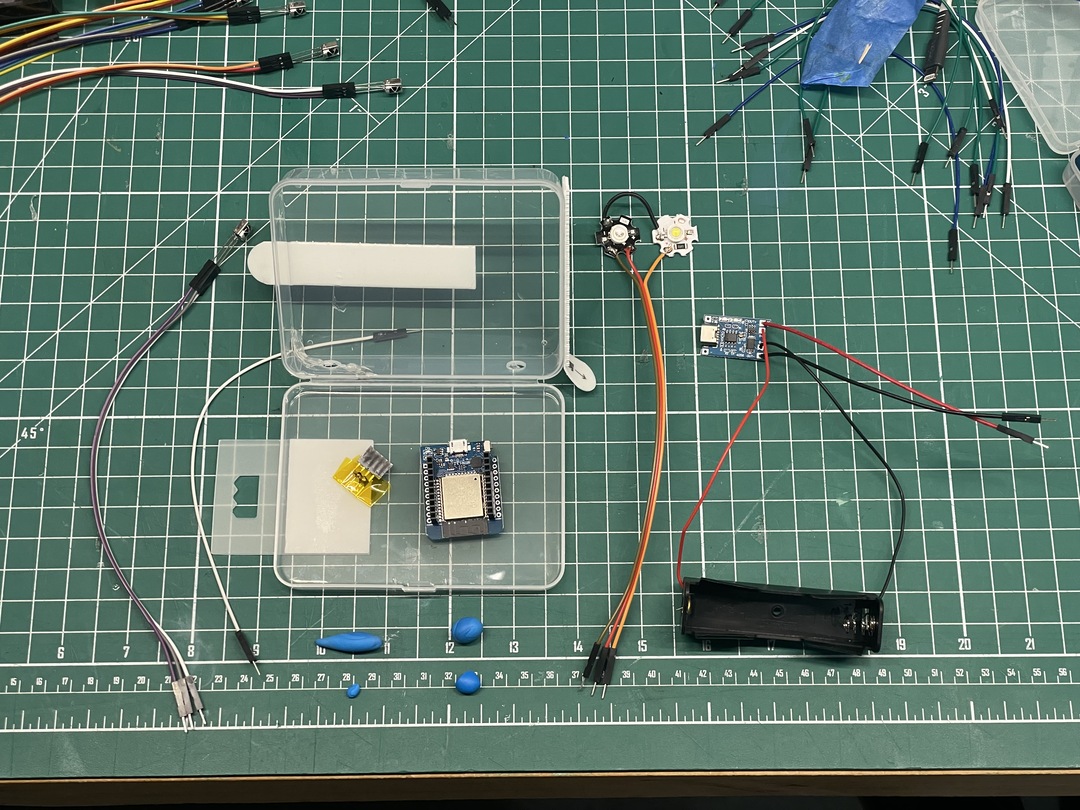 A small project setup featuring an ESP32 board, battery pack, and connected LEDs on a workbench.