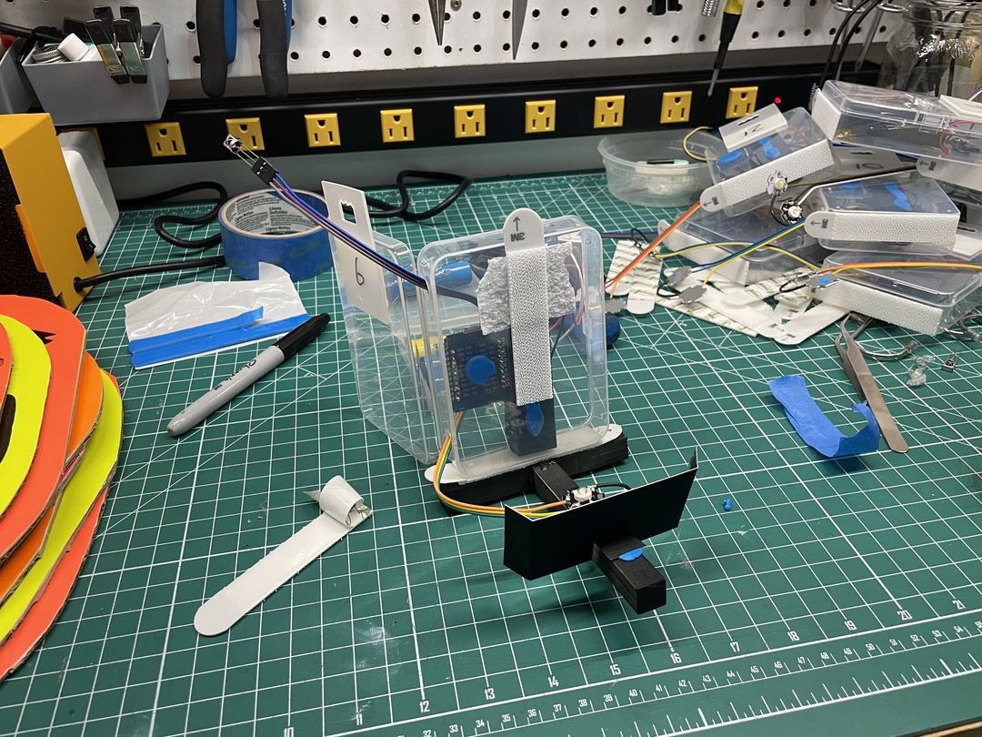 Prototyping station with a plastic container holding electronics, including a sensor module and wires.