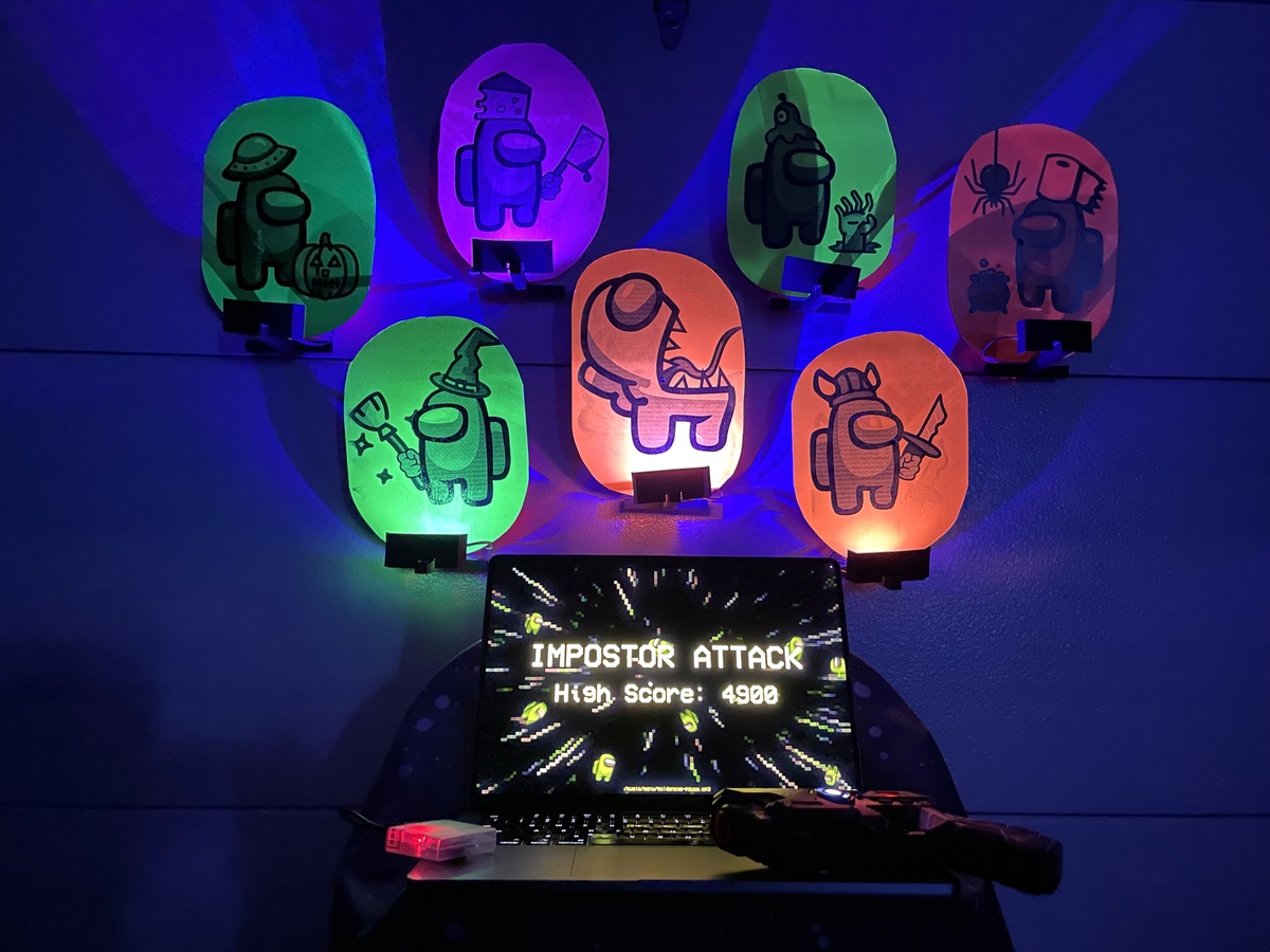 A custom gaming setup featuring Among Us-themed glowing targets in various designs, a laptop displaying the game "Imposter Attack" with a high score of 4900, and infrared components, all illuminated under colorful lighting.